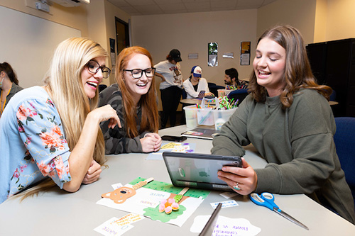Three students engaged in conversation at a table, using a tablet for discussion or collaboration