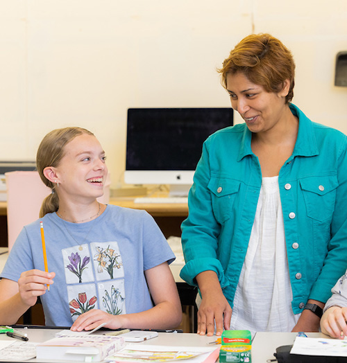 A woman teacher and two girls are seated together at a table, engaged in conversation and enjoying each other's company