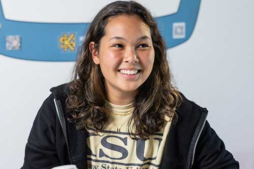 A photo of a Bagwell College of Education student wearing a KSU shirt and sitting at a desk and smiling