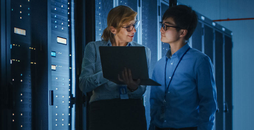 A cybersecurity instructor and a Kennesaw State students observe servers in a data center, highlighting hands-on learning