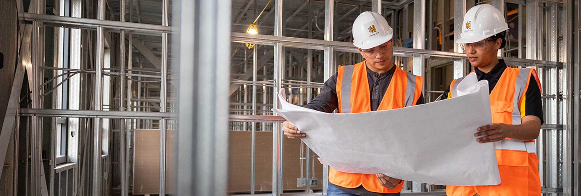 Two construction management students from Kennesaw State study blueprints in a partially built structure, highlighting their project planning