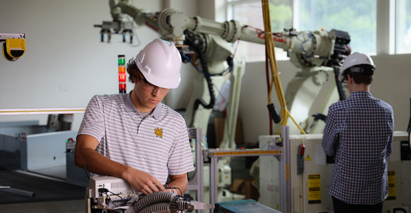 Two students engage in a robotic arm operation within a factory environment at Kennesaw State Southern Polytechnic College of Engineering.