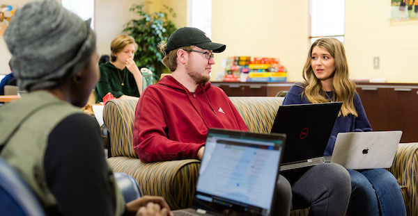 Students at Journey Honors College collaborate on laptops in a library setting, engaged in academic work and discussion.