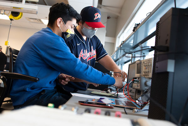 two students working with electrical engineering components on project