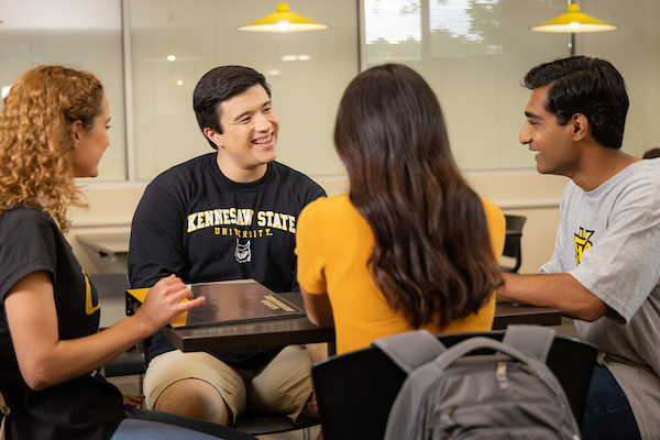4 students sitting around a desk and talking to each other