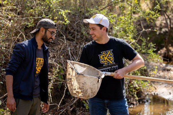 Two KSU students standing by a stream and one student holding a fishing net.