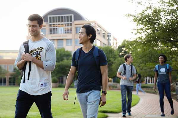 Students at Kennesaw State walking on campus, with Kennesaw Hall in the background.