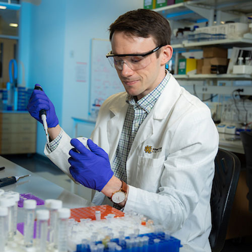 A KSU student researcher in a lab coat engages with a test, exemplifying the application of scientific methods in technology