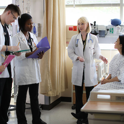 Doctors converse with a patient, providing guidance to student interns in a hospital environment