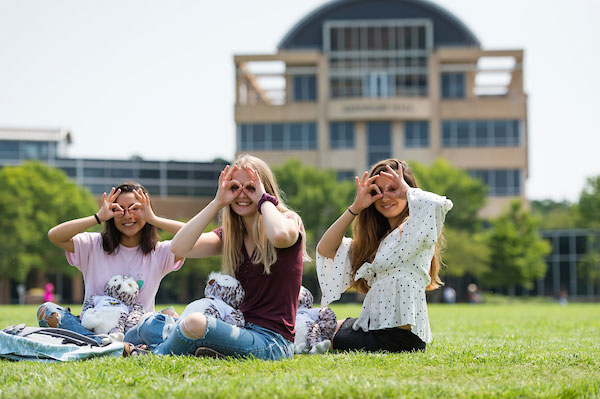 Group of students  giving owl eys on the Kennesaw State campus green with Kennesaw Hall in the background