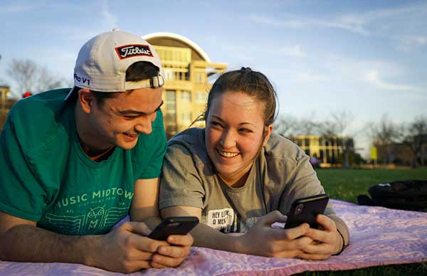Two Kennesaw State students lie on the university lawn, absorbed in their phones, enjoying a peaceful moment outdoors