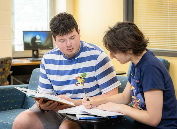 In a library, two Kennesaw State students engage in study at a table, immersed in their academic work.