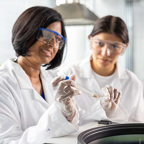 ksu professor and student wearing lab coats and safety goggles working together in a science lab, examining a test tube.