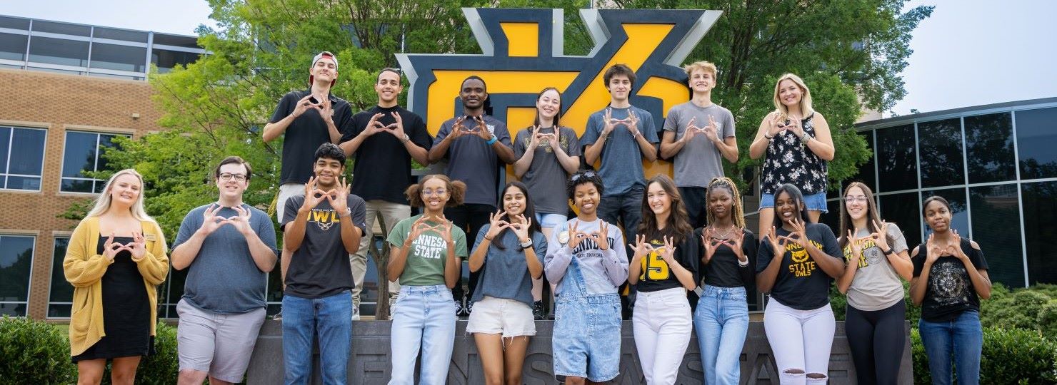 KSU Honors College students posing in front of the KSU statue on campus, making hand signs