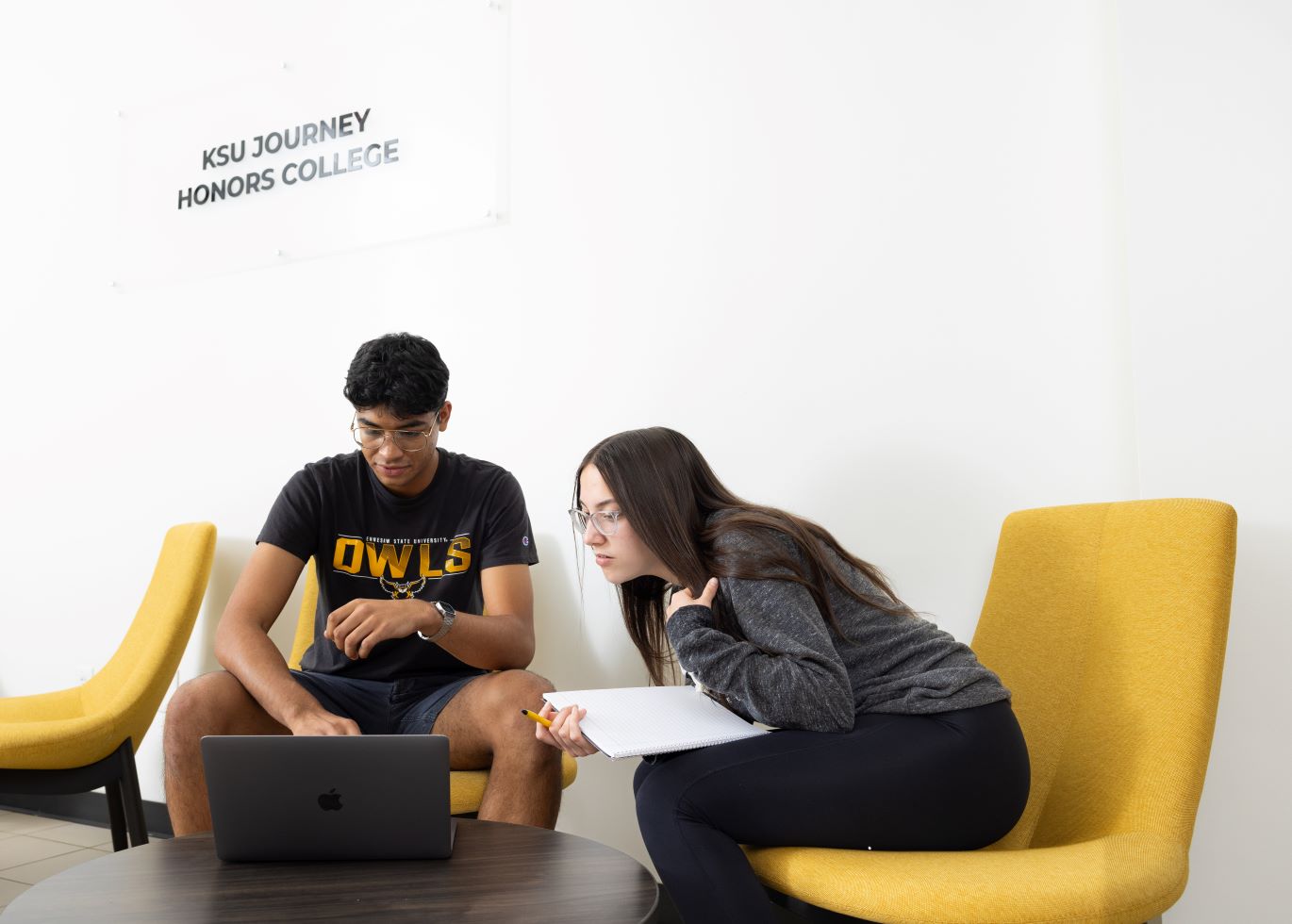 Two students studying together with a laptop and notebook in a lounge area