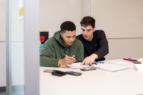 Two people working on homework together at a table with notebooks and calculators