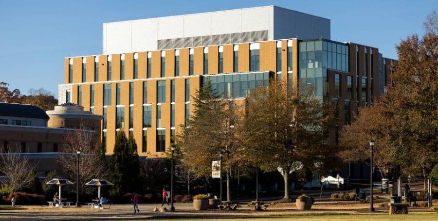 Modern multi-story building on KSU campus with brick and glass facade, surrounded by trees and grass.