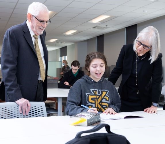 Student in KSU hoodie talking with two people in a classroom setting