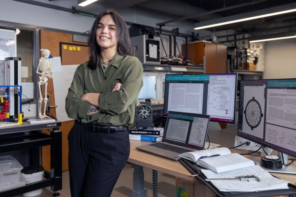 Person standing in a lab with monitors, books, and a skeleton model