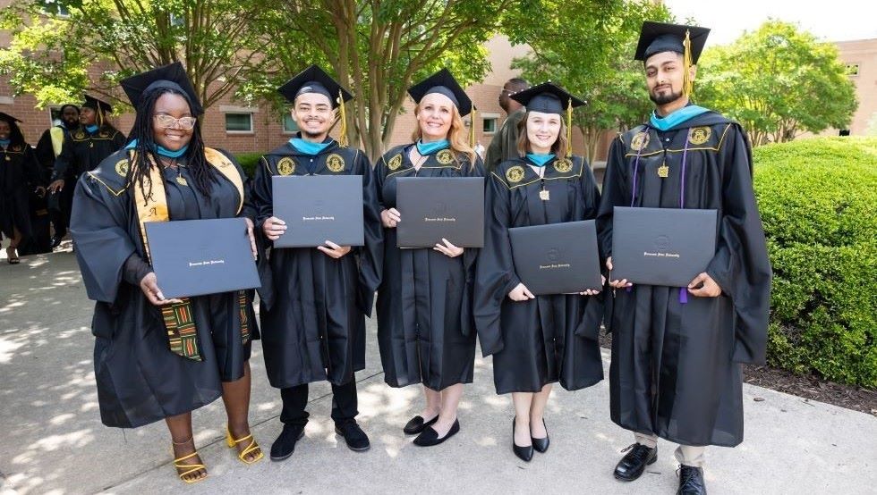 KSU graduates wearing caps and gowns while holding diplomas