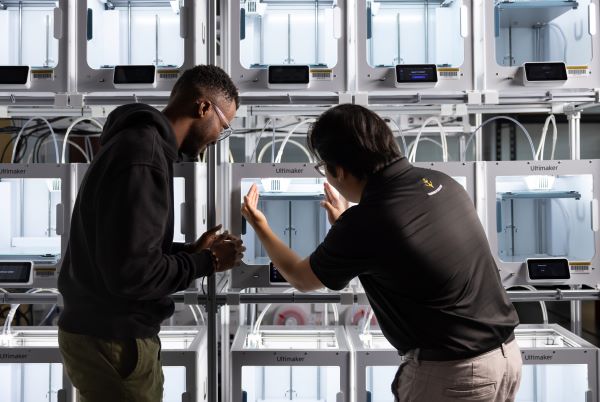 Two people in front of a wall of Ultimaker 3D printers