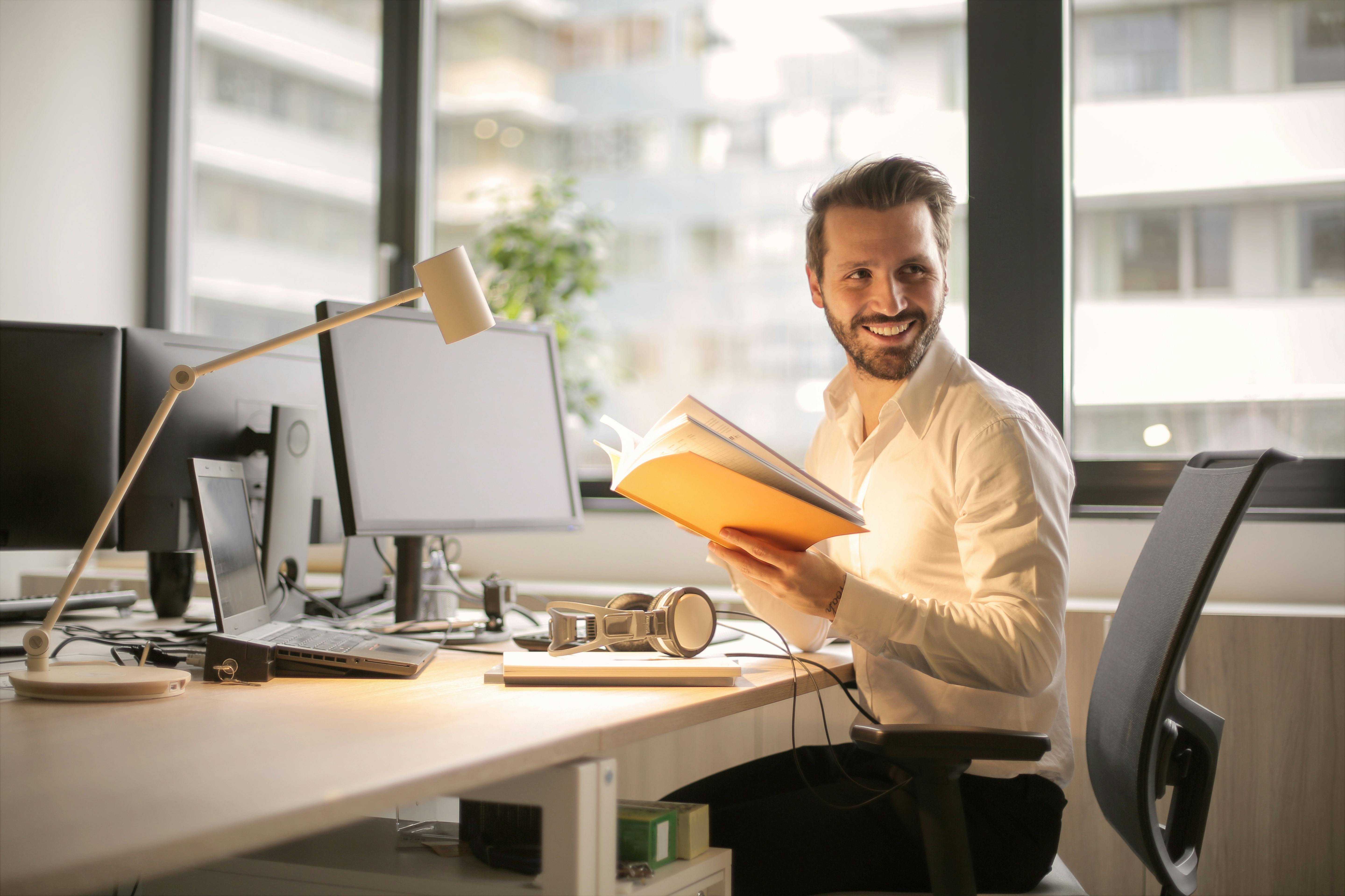 guy holding folder as his smiles and turns his head at office desk