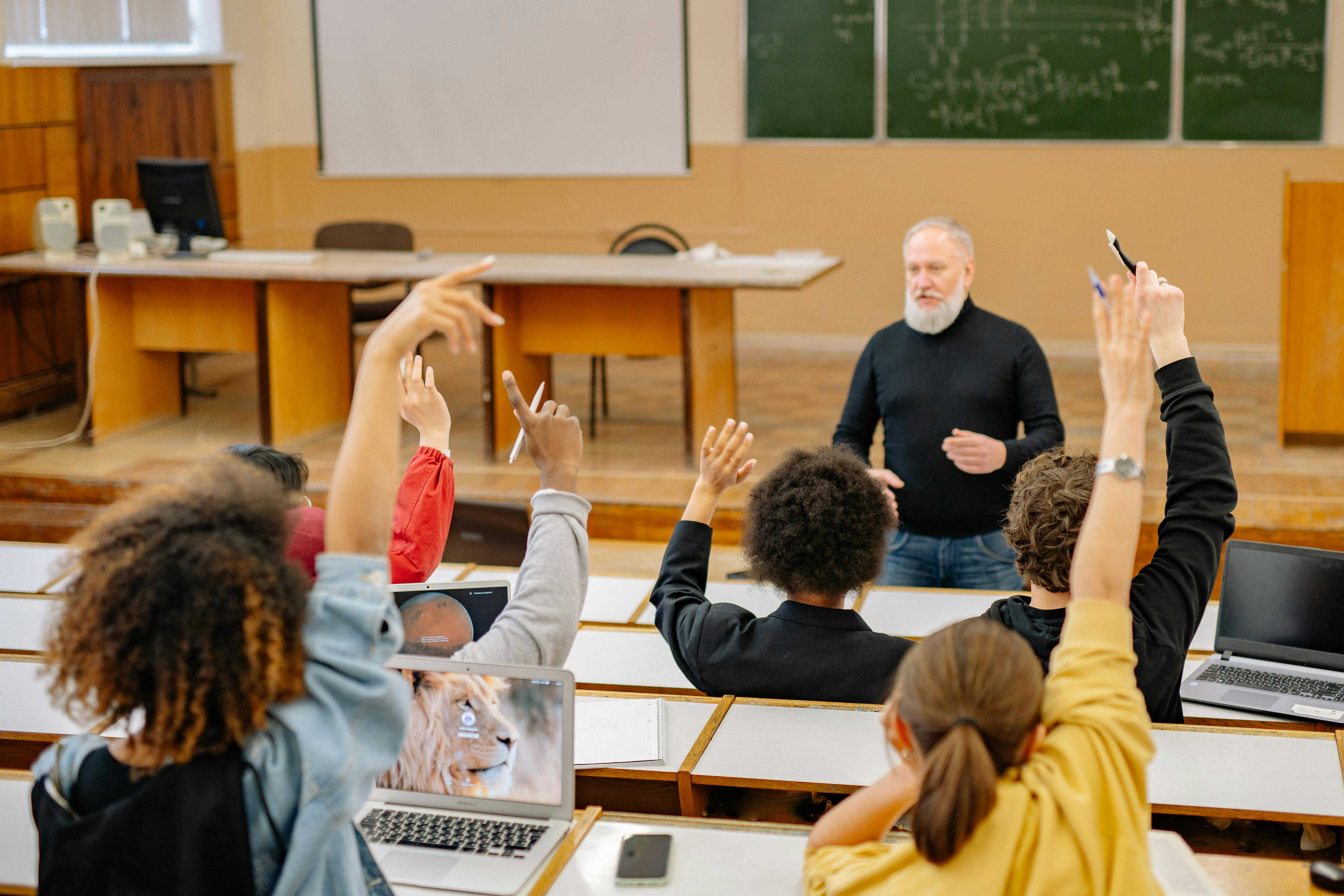 group of students raising their hand in class with male older teacher
