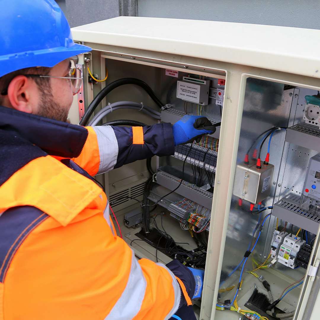 male engineer with blue hat and orange suit working on electric device