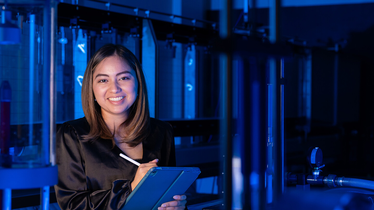 girl in blue computer lab smiling in a black silk top as she holds a pen and ipad