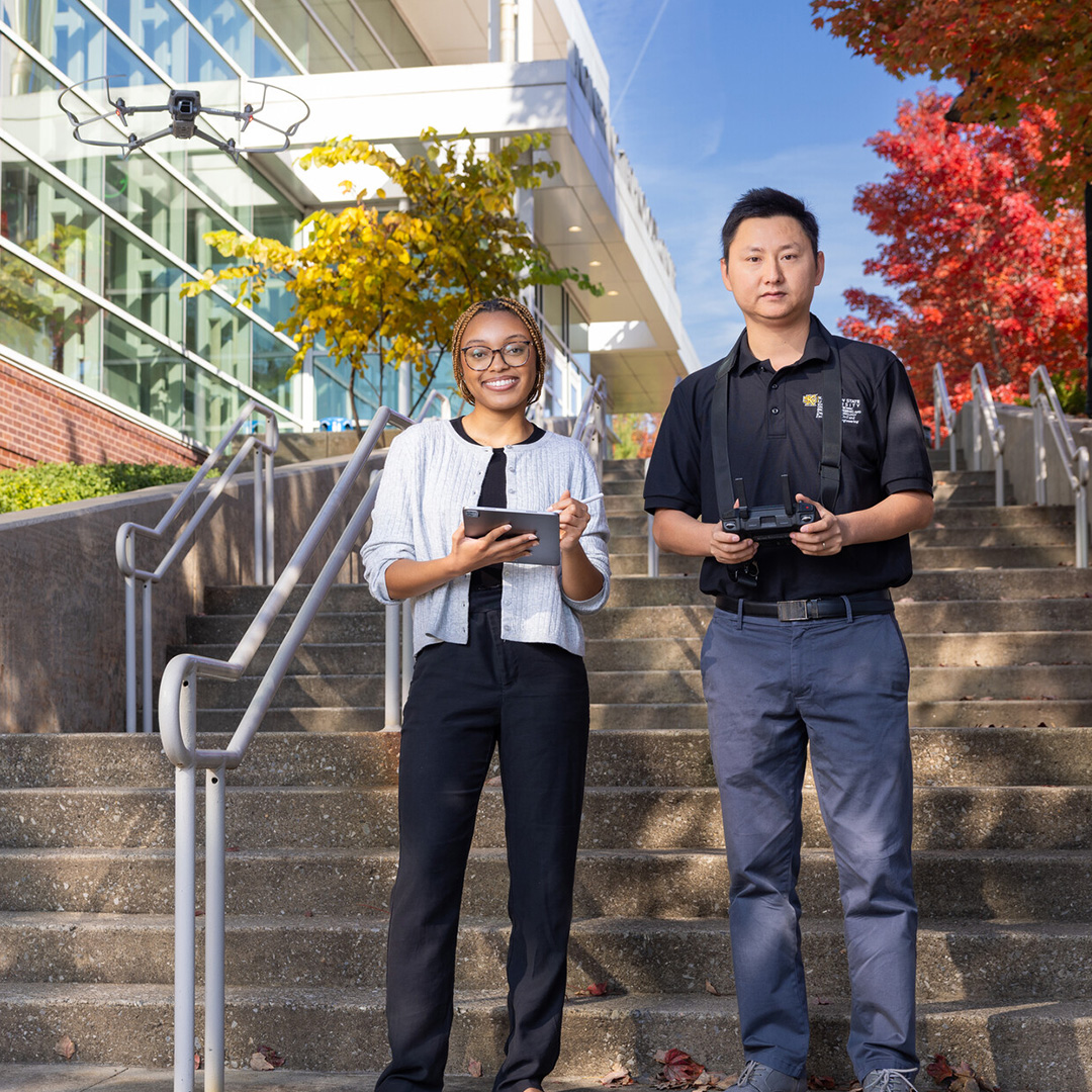 two people standing on steps operating drone camera in the air