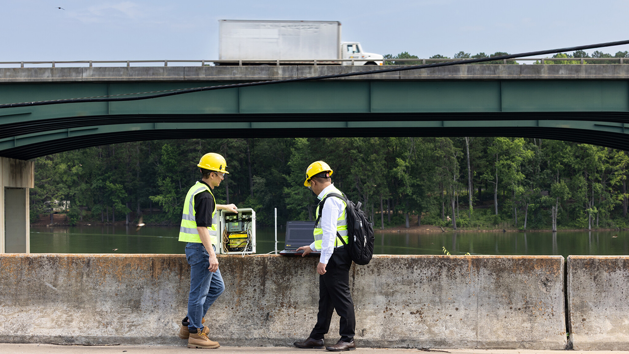two constuction workers with yellow hats talking over bridge