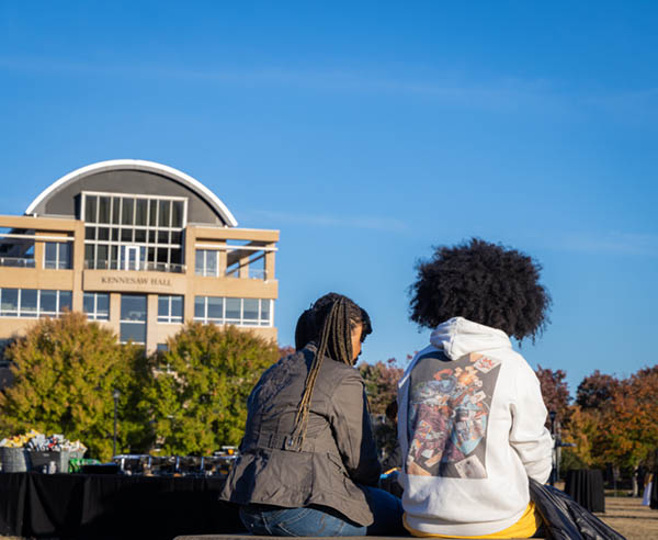 Son and mother sit together on bench looking out over the KSU beautiful green campus