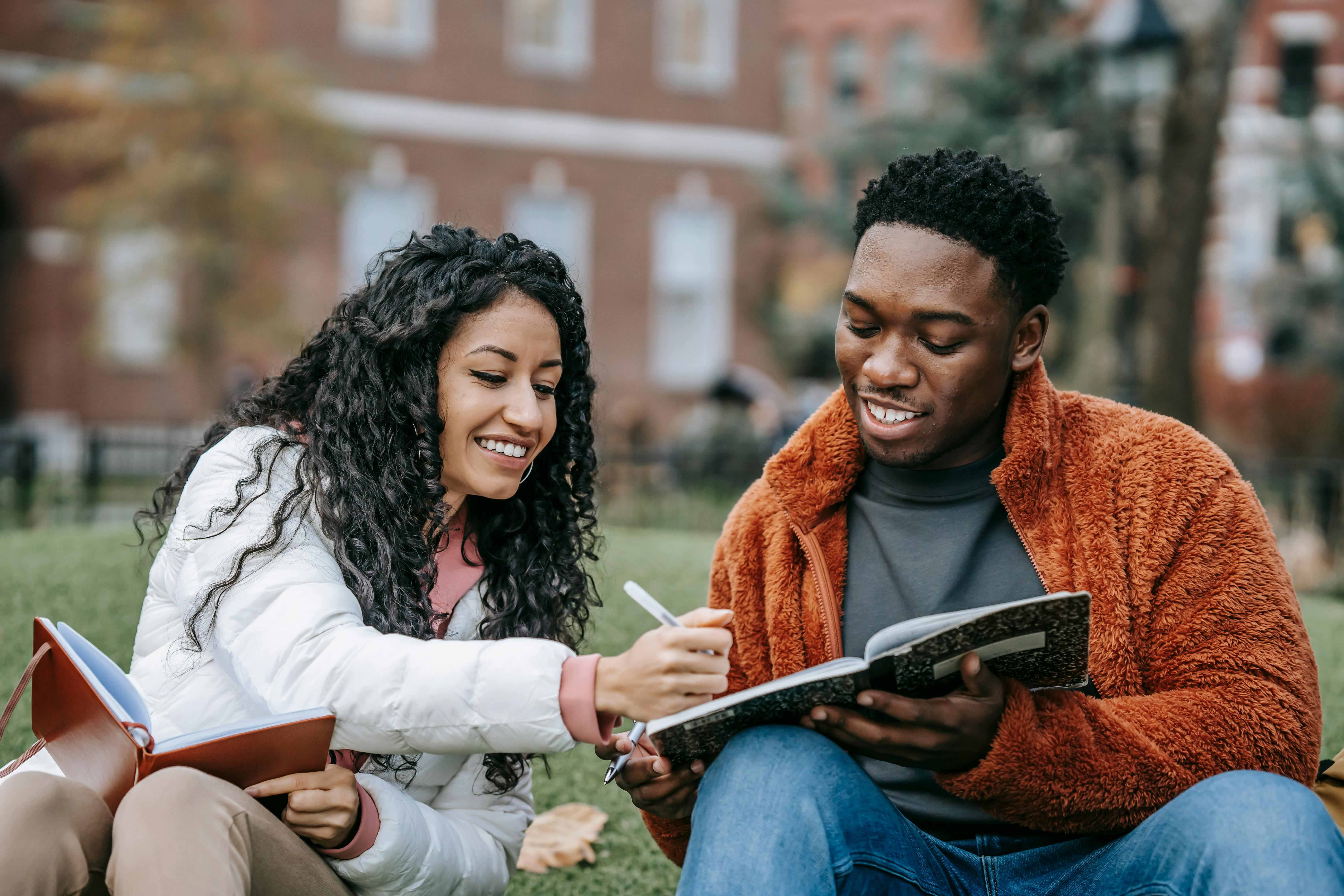 female and male student sitting on grass while they study
