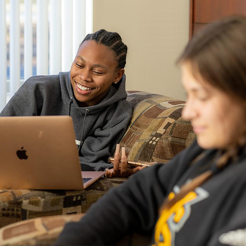 two students on couch as they do homework on computer