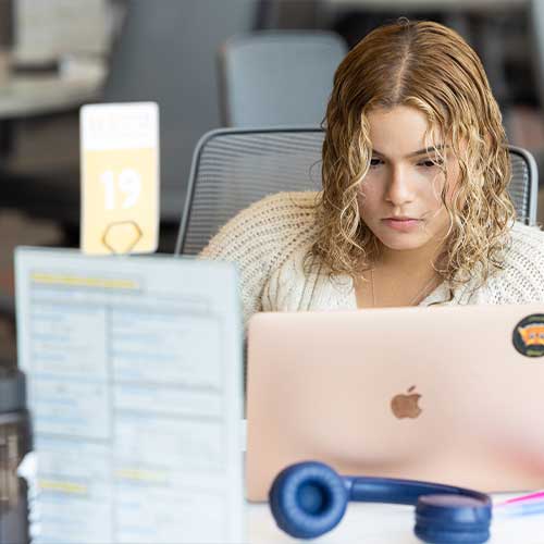 KSU student sitting at a table focused on laptop.
