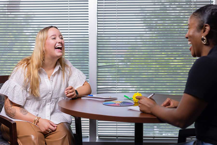 high school student and counselor sitting at a table laughing together.