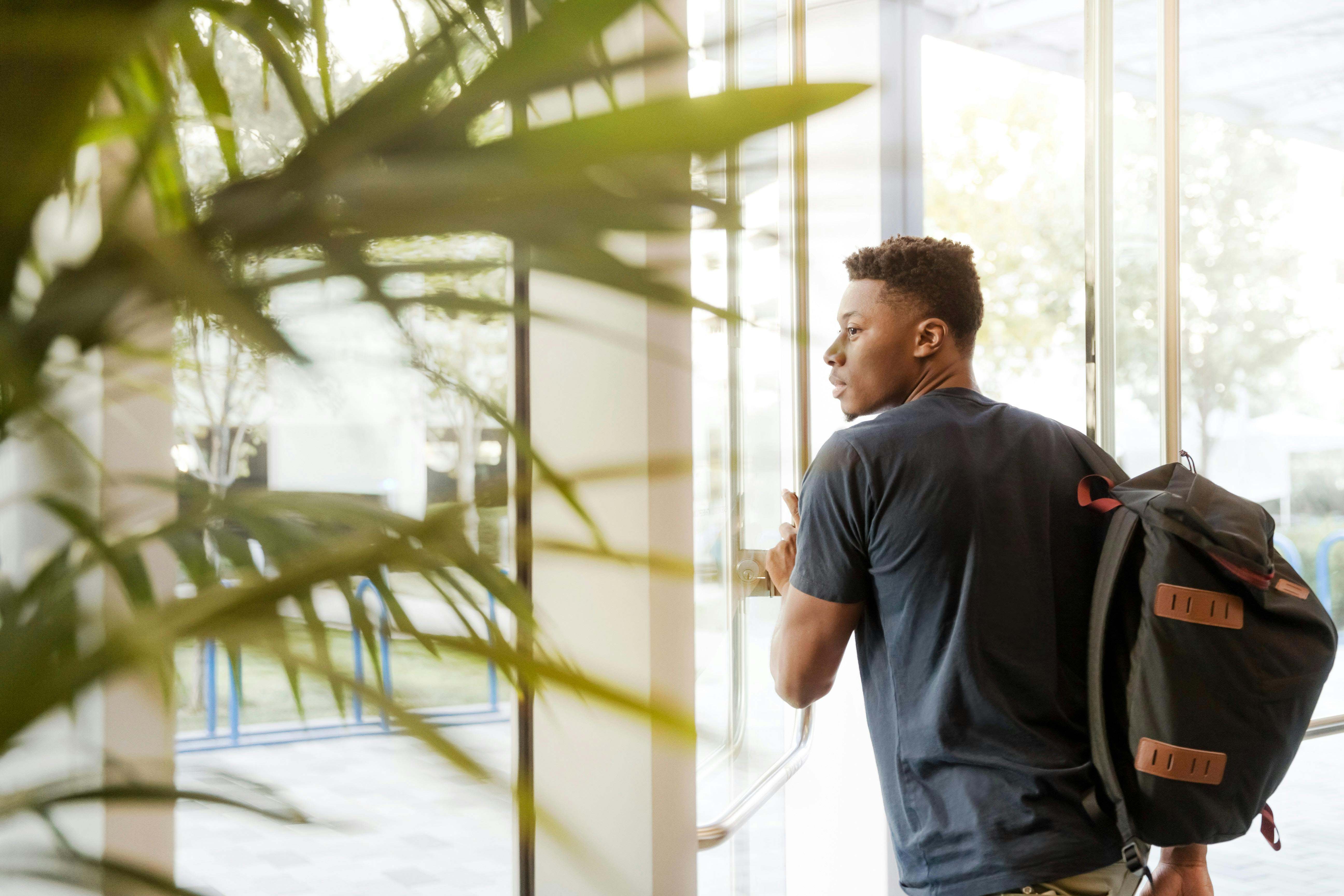 male student with backpack heading through door next to plant