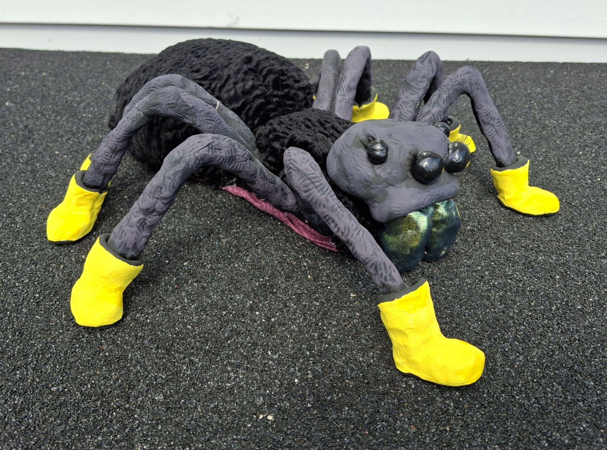 Black spider model with yellow boots on a textured black surface. / Soft sculpture example for Sculpture 1 class. The students learned to use a sewing machine in this lesson. 