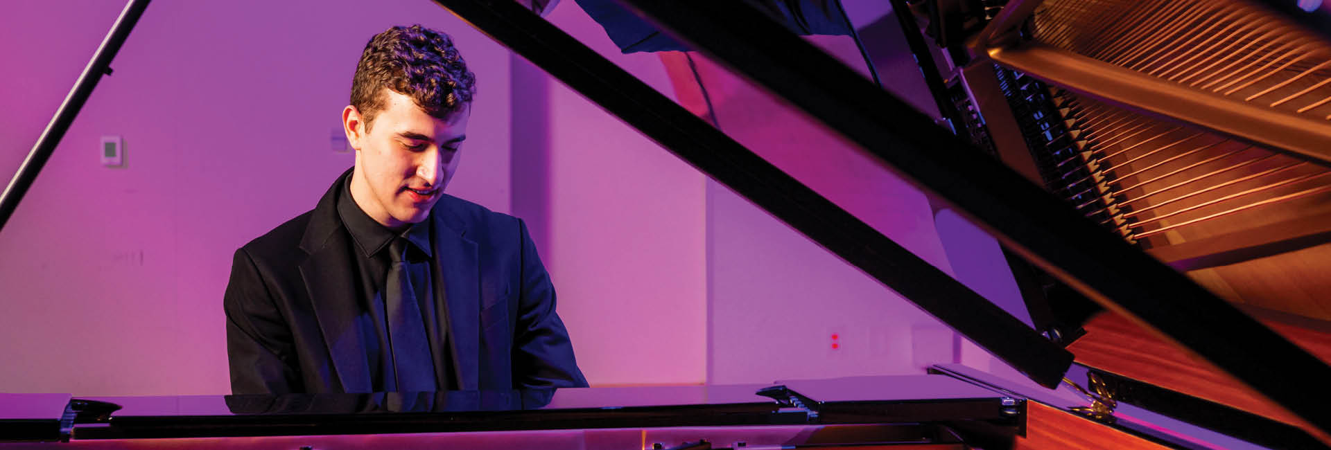male student playing piano in suit attire