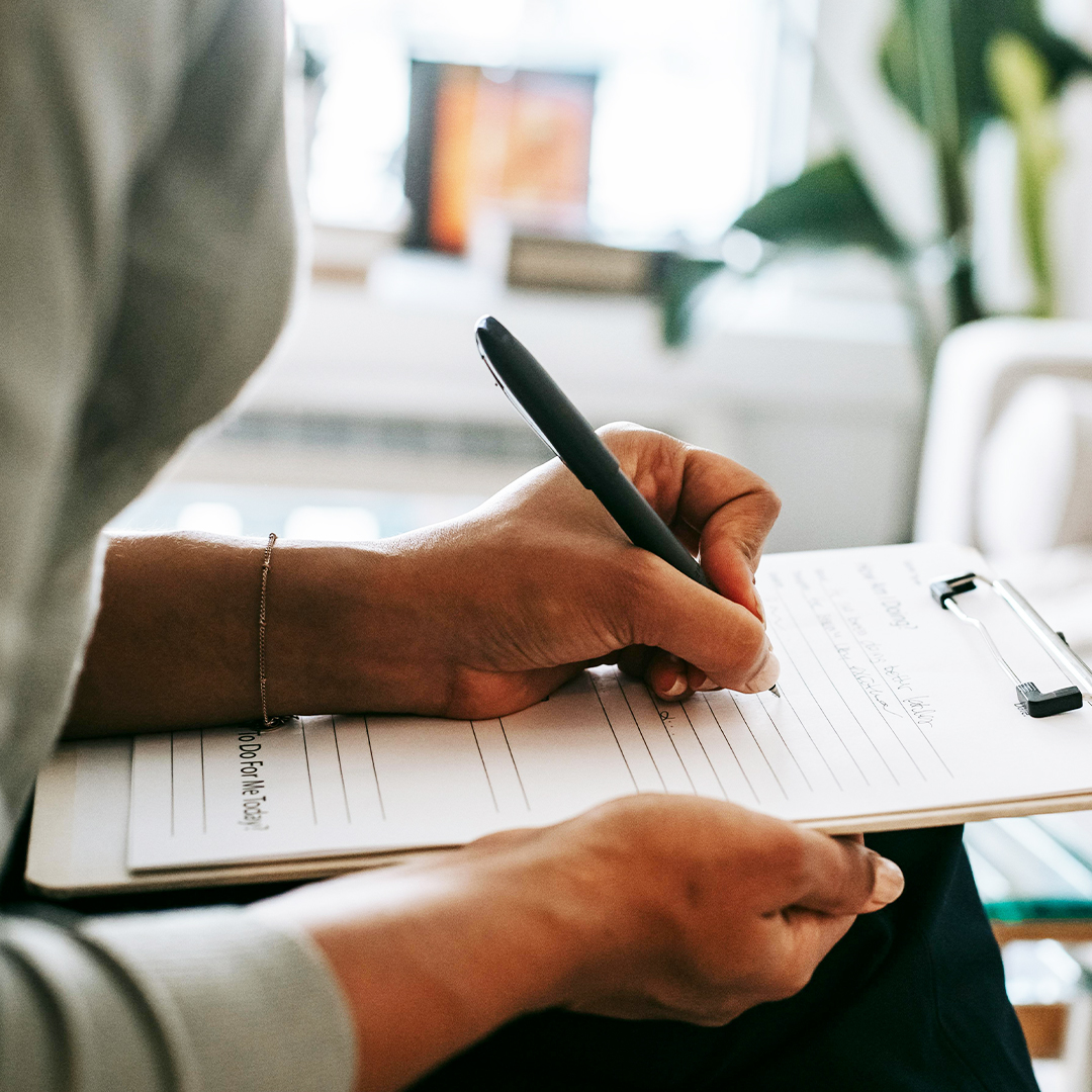 hand holding pen while writing on paper to register for event