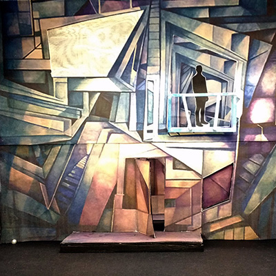 set design constructed from multi-colored paper with cutout of man seen in window, standing on top floor
