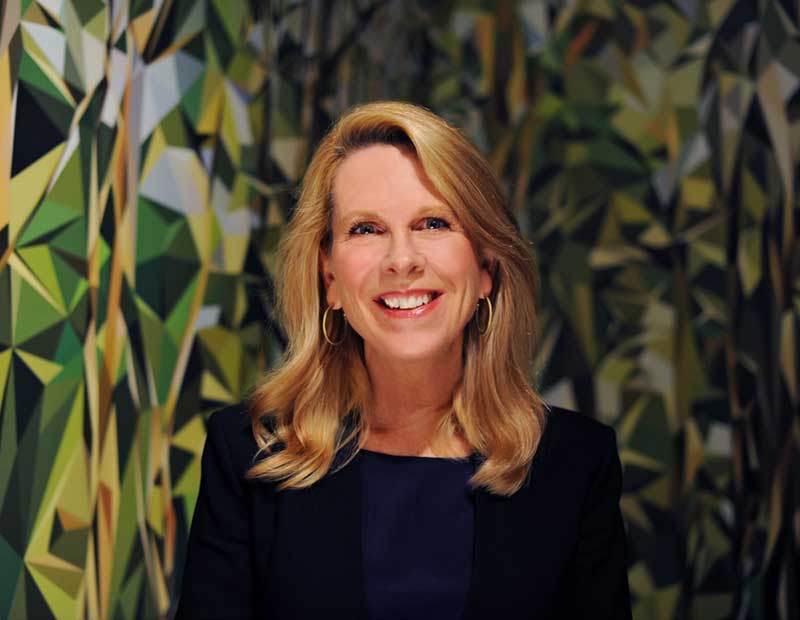 image of Alice Gray Stites smilling in front of a color geometric background of green, black, and tell triangular shapes