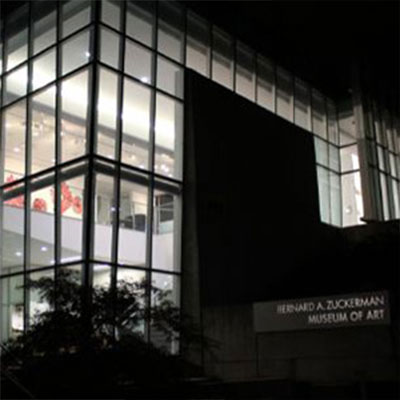 Night time photo of the Bernard A. Zuckerman Museum of Art's exterior building facade detailing the large glass corner window grid