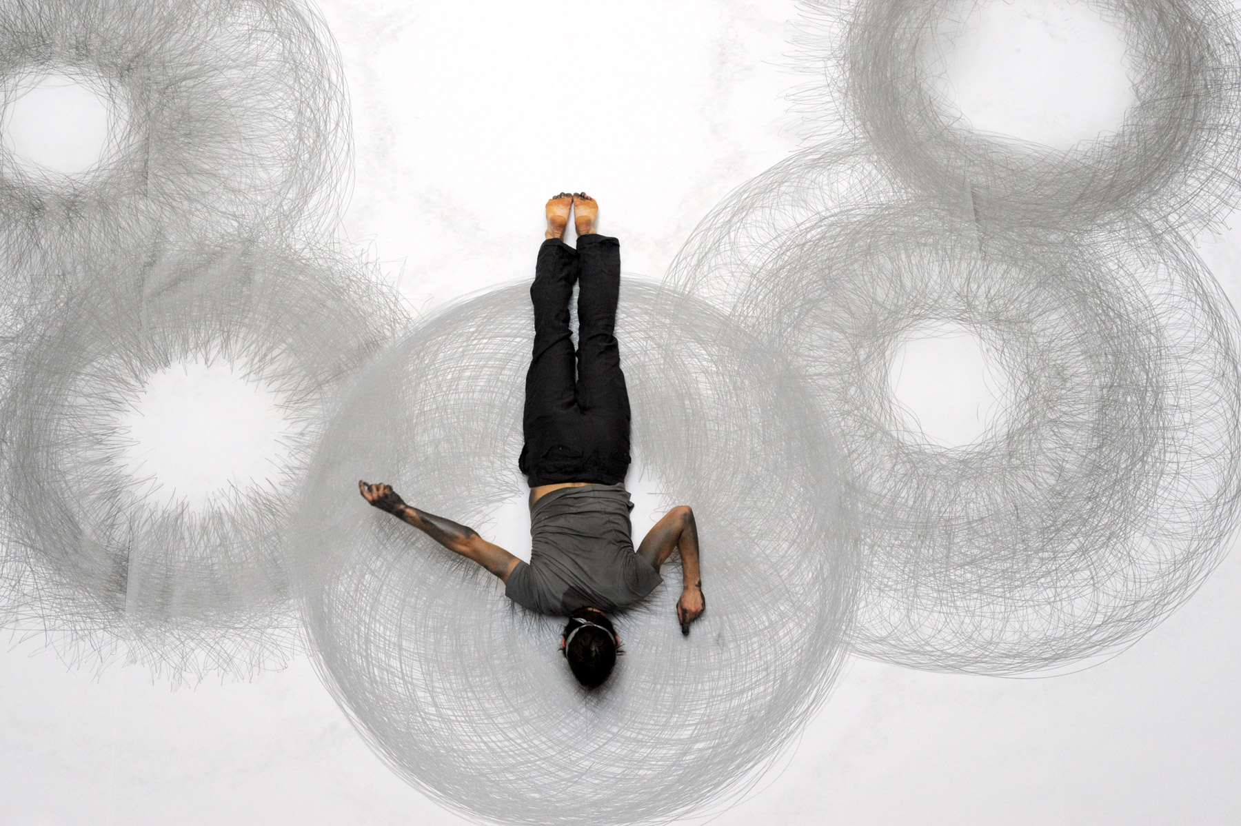 Photo of artist Tony Orrico performing 8 Circles. The artist is seen face down with arms in motion, covered in graphite. 