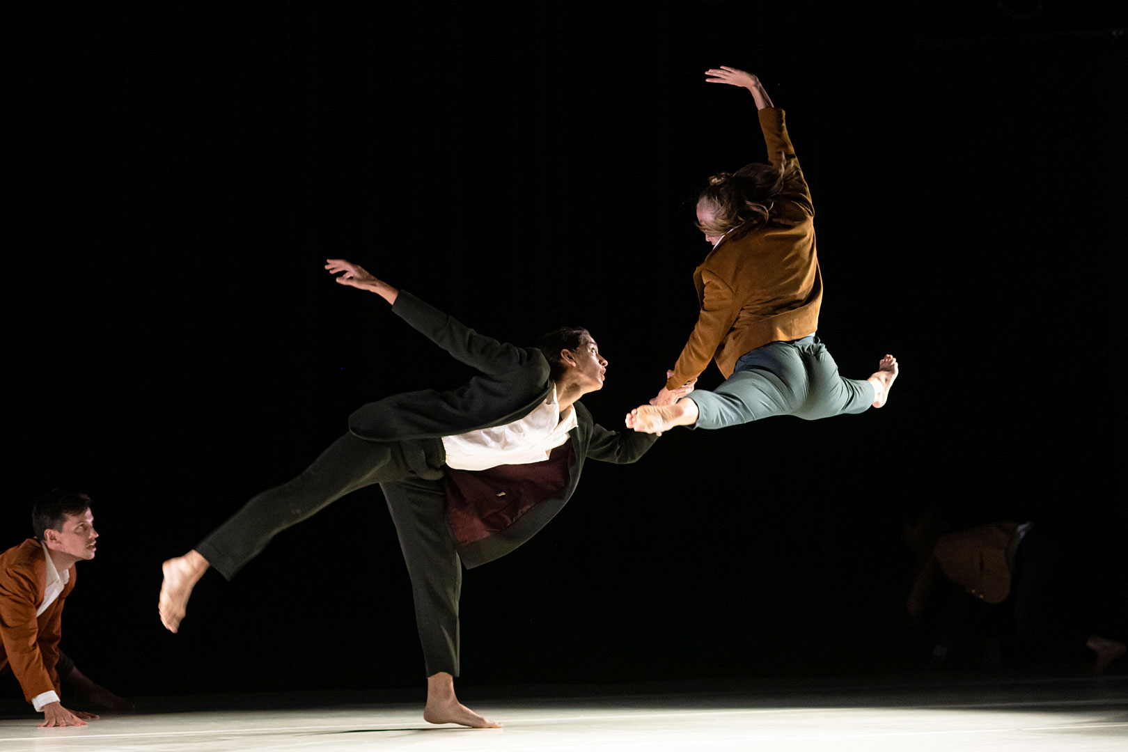 image of dancer jumping in the air, with a man crawling to stop them