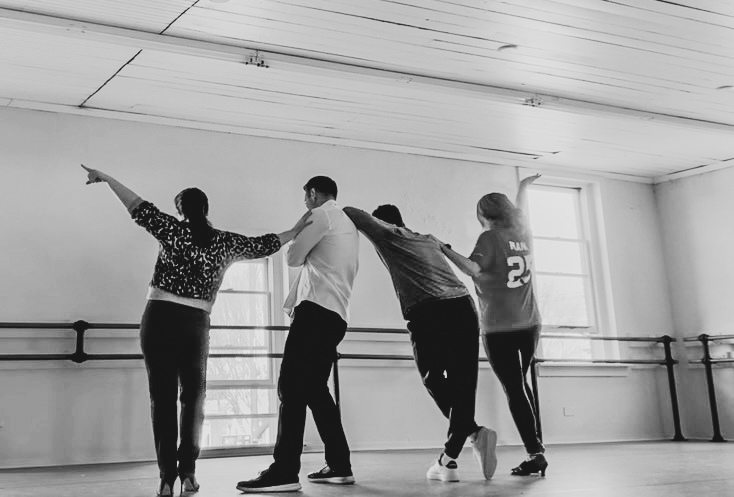 four dancers stand with their backs to the camera