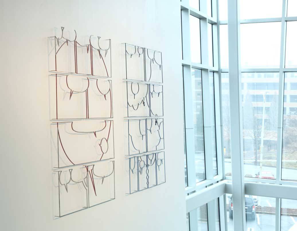 Image of Greely Myatt's installation at the ZMA featuring "Untitled Pages (Hagar) and (Beetle Bailey) created in 2011 with Painted and polished steel and air, measuring 73 x 53 x 3" each. The two "pages" created by the artist are installed side by side on the wall. (Hagar) on the left features multiple steel frames of different sizes in 4 rows. All eight frames feature different sized thought bubbles. The thought bubbles come together to create an abstracted smiley face on the work on the left. (Beetle Bailey) on the right features ten different sized frames arranged into four rows. The motif in this untitled page consists of several small thought bubbles throughout and three larger thought bubbles that interact in multiple frames.  