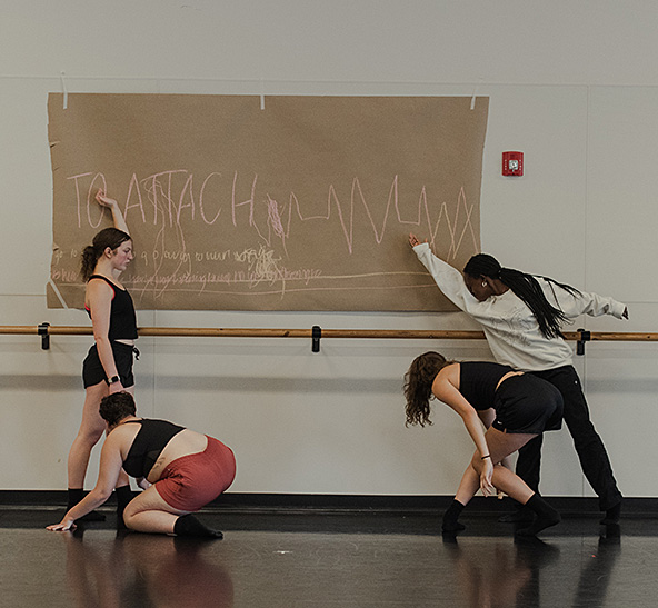 image of dancers with a piece of paper taped to the wall they are writing on