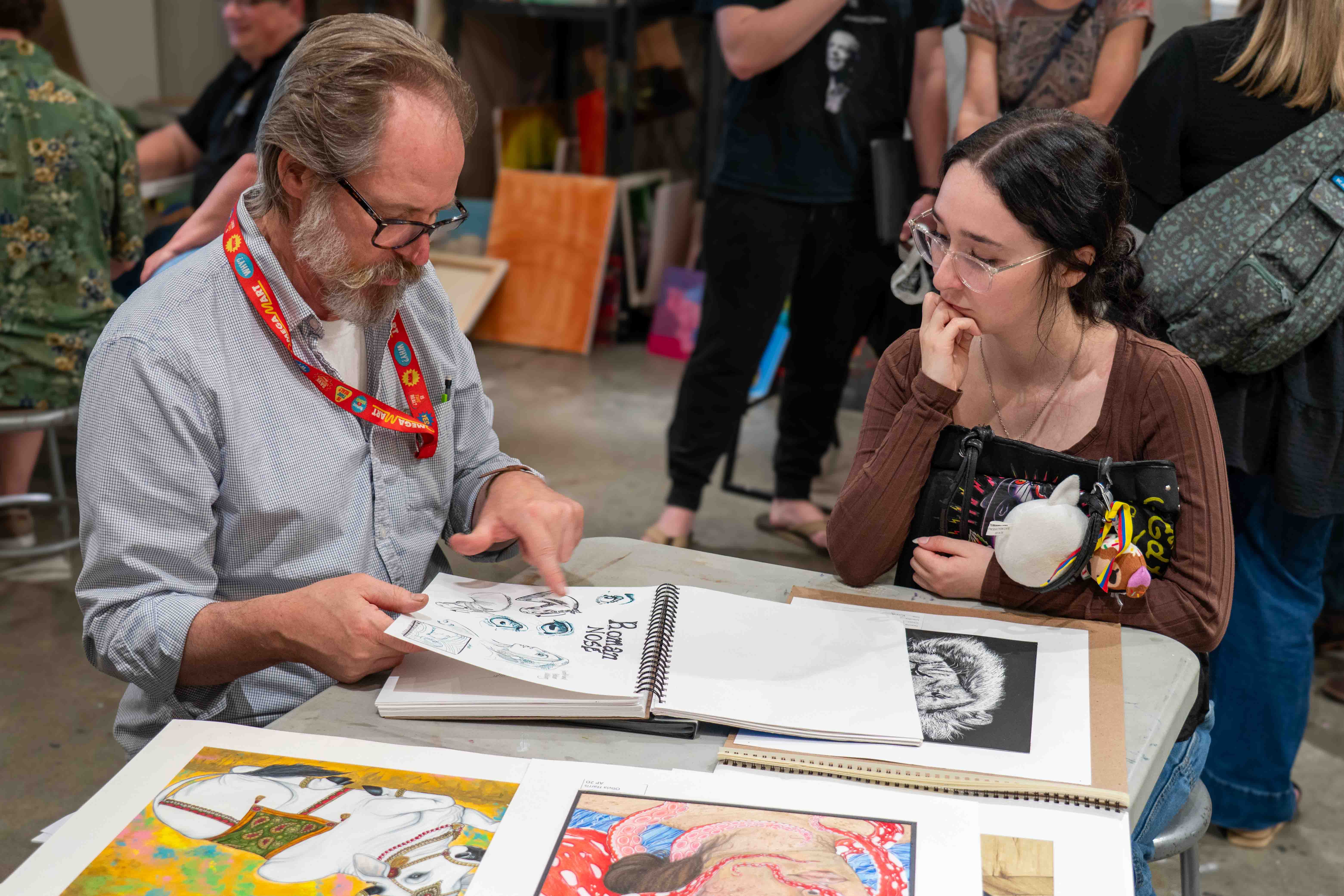 Professor sitting with a student reviewing her artwork.