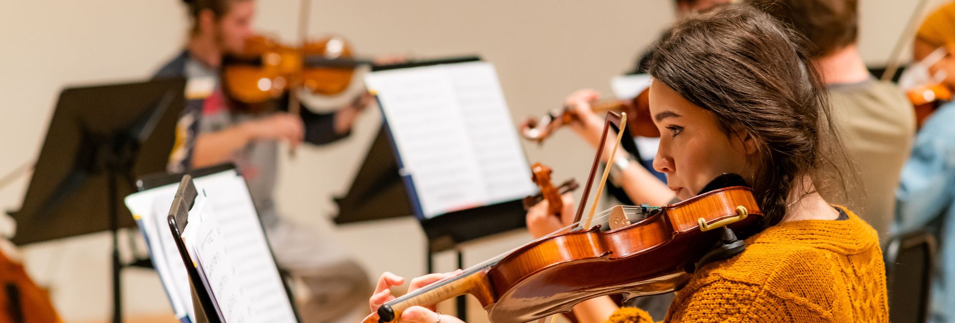 image of female student playing violin with other string players in the background
